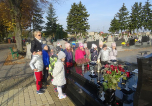 Grupa dzieci z panią Arletą przygląda się grobom księdza Bogusława Palenickiego oraz księdza Ryszarda Kolibskiego, w tle inne groby.